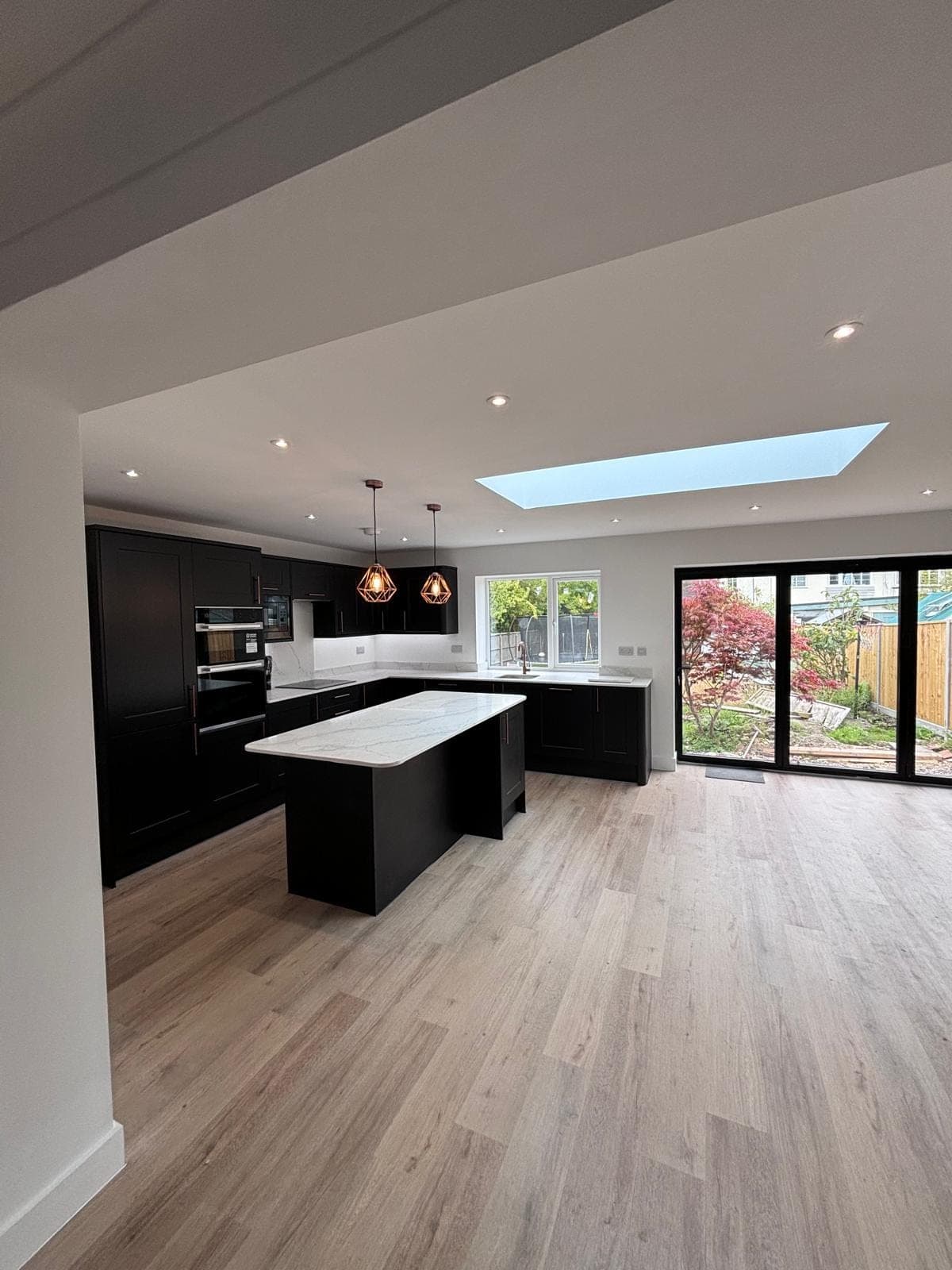 Open-plan matt-black kitchen extension with a roof lantern and bi-fold doors to the garden